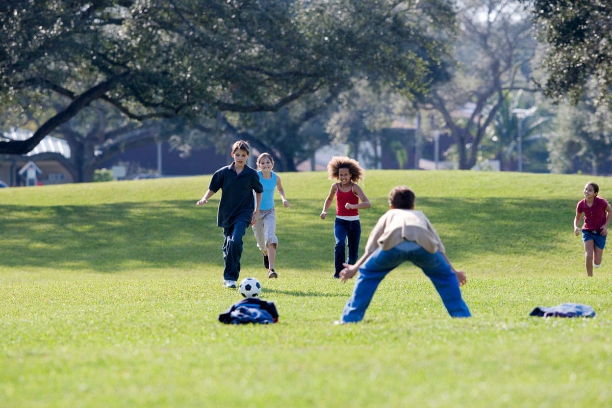 Children running across an open grass field on a bright day