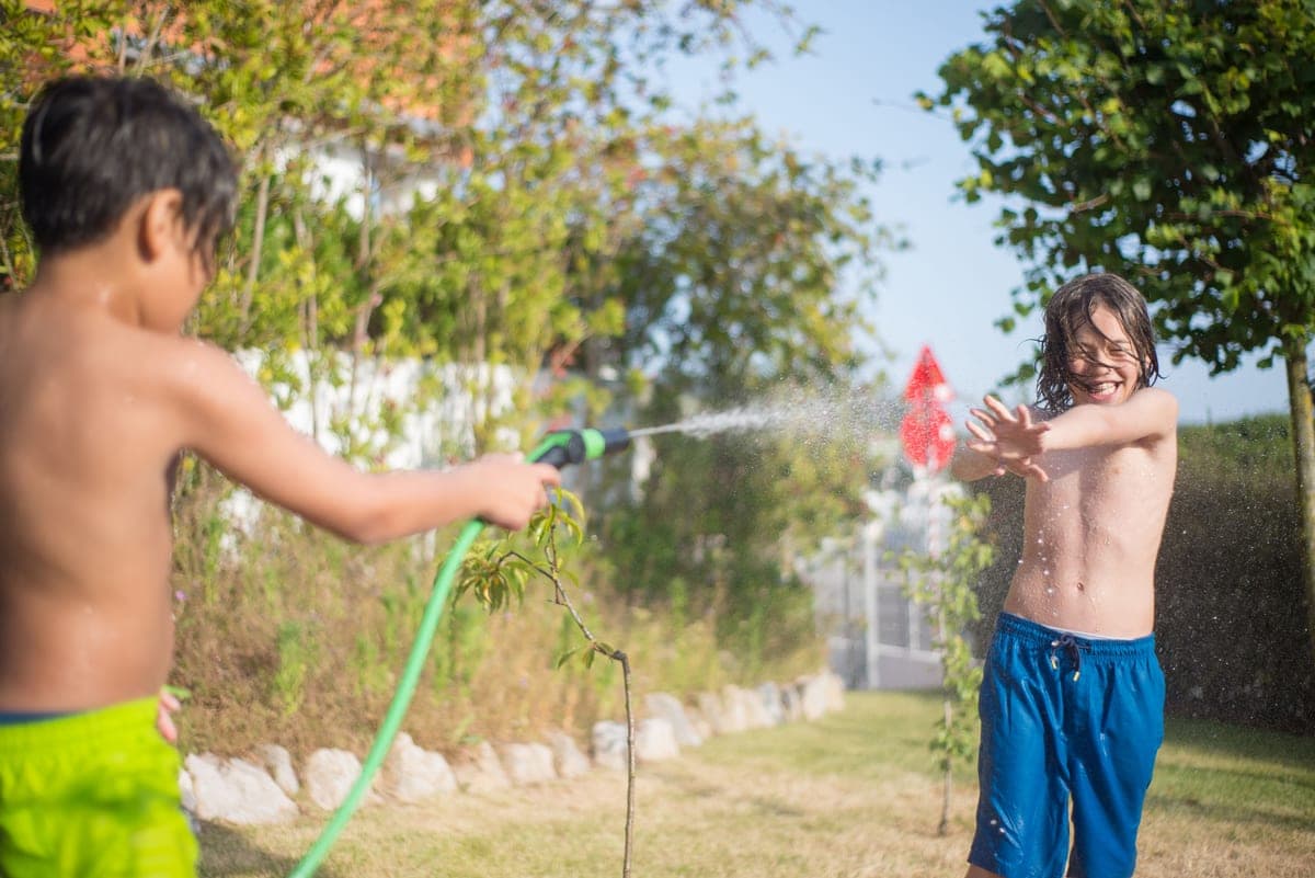 Children running through a garden sprinkler on a hot summer day